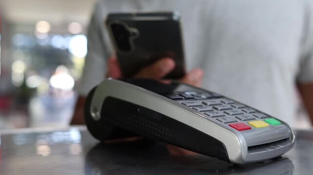 Customer completing a secure digital transaction using contactless payment with a smartphone on a pos terminal at a checkout counter