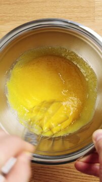 Chef whisks egg yolk and sugar in metal bowl, timelapse. Pale mixture forms rich custard base for vanilla ice cream. Add cream, milk and vanilla before churning smooth gelato or frozen dessert.