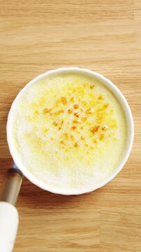 Person caramelizes sugar with kitchen torch over ramekin. Safety lesson shows steady grip, controlled flame and workspace. Torch use keeps hands away from heat while creating golden dessert crust.