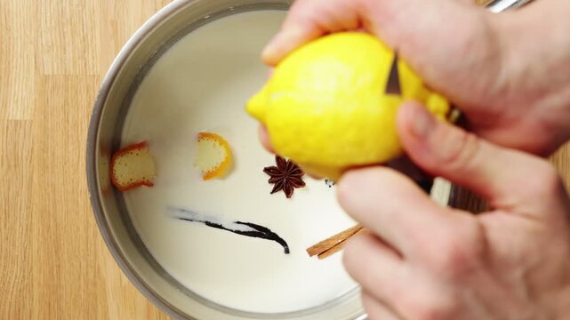 Pastry chef's hands cut and add lemon peel to milk mixture. Citrus-infused dairy creates fragrant pastry cream for lemon tart. Custard fills French tartlets, eclairs, choux buns or layered desserts.