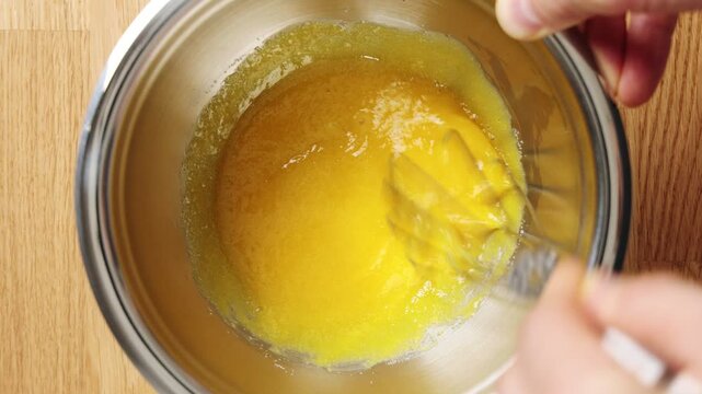Person whisks egg yolk and sugar in metal bowl, timelapse. Sweet yolk foam forms tiramisu base with mascarpone. Traditional Italian dessert layers coffee-soaked ladyfingers, cream and cocoa.