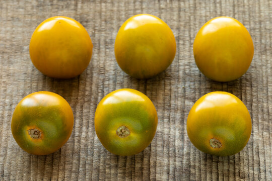 Six rare heirloom Green Grape Cherry tomatoes are displayed on a rough wooden background. Ripe, homegrown, organic green tomatoes backlit by natural window light.