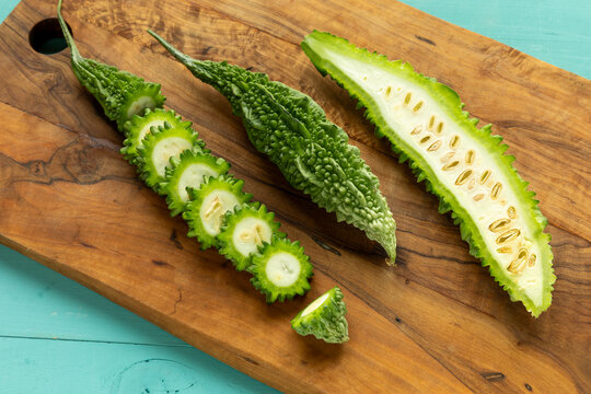 Bitter melons on a cutting board, with one whole, one halved, and one sliced.