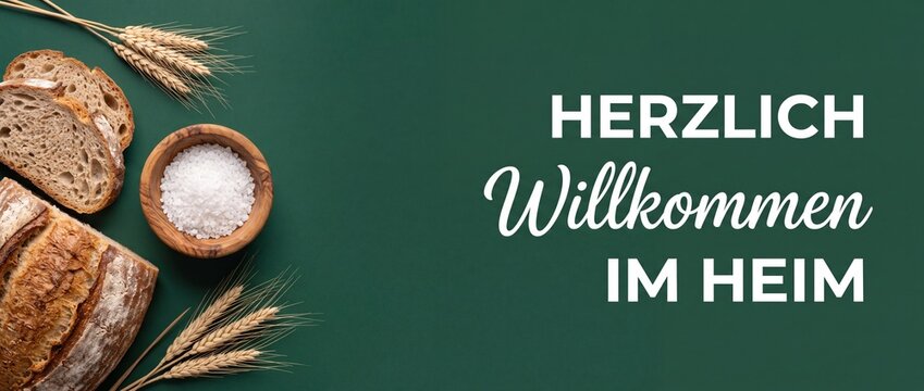 Fresh sourdough bread and salt on green background with German text Herzlich Willkommen im Heim for traditional housewarming greeting card, banner background copy space for new home concept design.