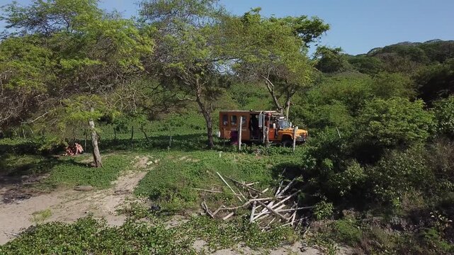 Drone reveal of yellow camper truck hidden in bushes with scenic sea shoreline and dense forest backdrop