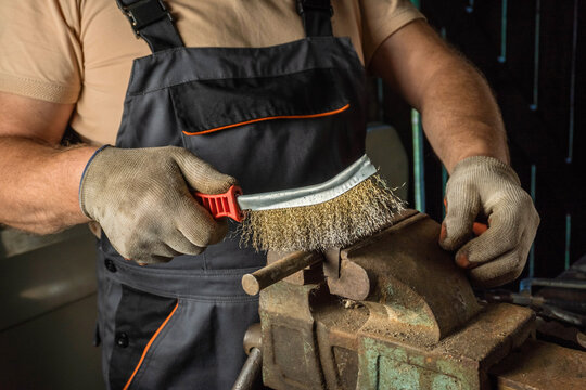 In a bustling workshop, a skilled craftsman focuses on cleaning his tools with a wire brush. The surrounding environment reflects a commitment to quality and precision