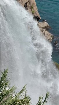 Lower Duden Waterfall plunges directly over a steep limestone cliff into the turquoise Mediterranean Sea, Antalya. The heavy, roaring white water stream splashes against coastal rocks