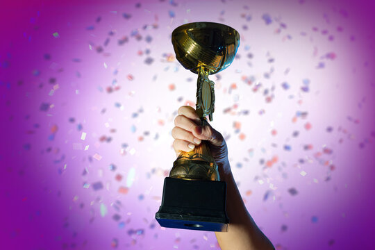 a woman's hand hand Raising Golden Trophy  cup  with Falling Confetti Background