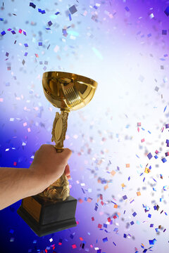 Hand Raising Golden Trophy with Falling Confetti Background