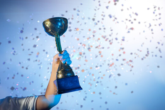 a child's hand Raising Golden Trophy with Falling Confetti Background