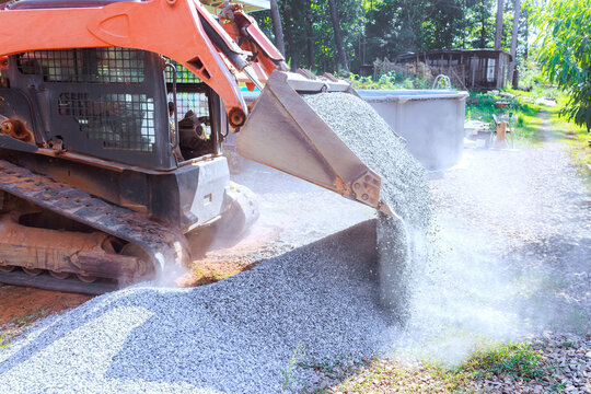 Construction vehicle pours gravel onto ground in residential yard