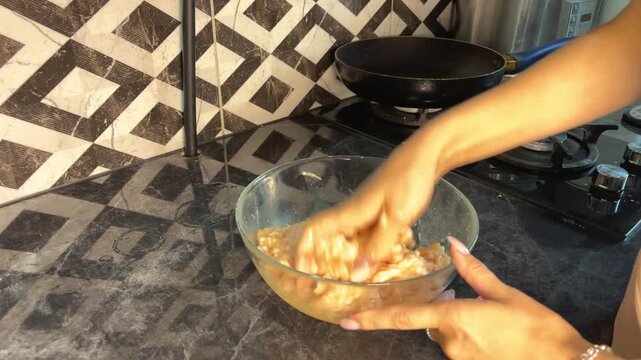 Hands knead seasoned ground chicken in a glass bowl while preparing homemade patties.