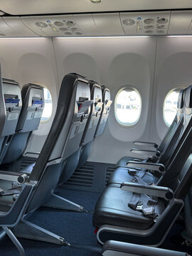 Interior view of an airplane cabin showing rows of black leather seats with seatbelts, large windows, and overhead compartments in a modern aircraft setting