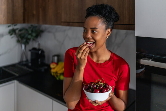 Black woman enjoying fresh cherries in modern kitchen healthy snack and happy moment