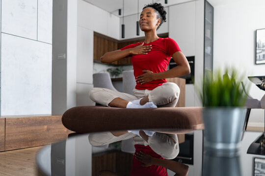 Woman practicing mindful breathing and meditation at home on a cushion in modern living room