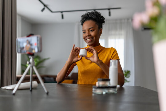 Woman recording beauty product review at home showing skincare jar on camera