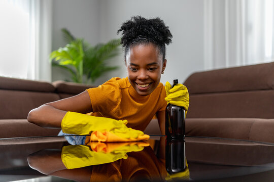 Smiling woman cleaning glass coffee table at home wearing yellow gloves