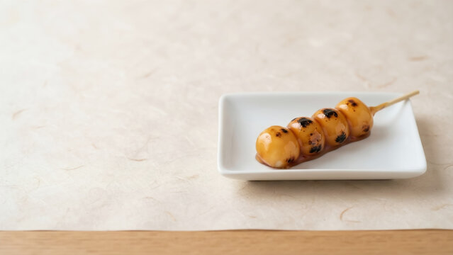 Delicious skewered Mitarashi dango with sweet soy sauce glaze on a white small plate over traditional Japanese washi paper with copy space.