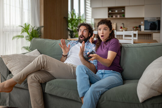 Caucasian couple on couch reacting with surprise while watching TV in cozy living room