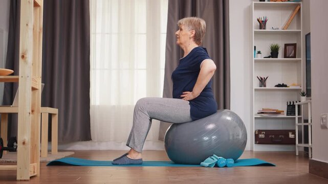 Senior woman sits upright on a stability ball during a home exercise routine, using controlled posture and balance as part of active fitness training to support mobility and balance training.