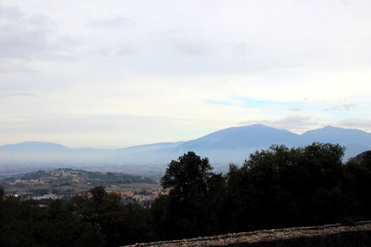 Spiritual scene from Spoleto overlooking the Spoleto Valley, dotted with small towns, villages and fields, with prominent, rolling, hazy blue massifs on the horizon, part of the Umbrian Apennines
