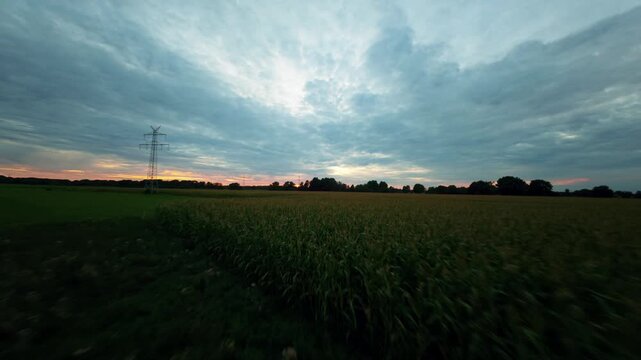 FPV-Drohnen-Tiefflug &uuml;ber Fluss und Maisfeld mit Aufstieg in einen dramatischen, dunkelorangen Sonnenuntergang