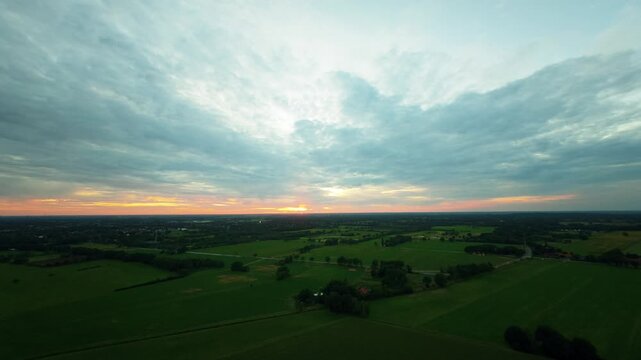 FPV-Drohnenflug aus gro&szlig;er H&ouml;he &uuml;ber weite l&auml;ndliche Landschaft mit Sonnenuntergang im Hintergrund