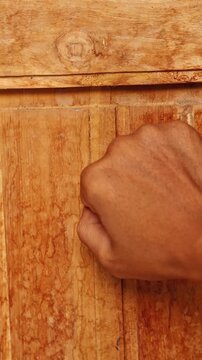 Close up of a hand knocking on an old wooden door, visitor arrival and hospitality home entrance concept.