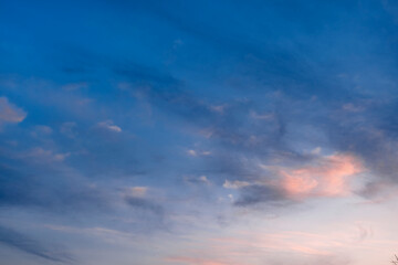Obraz premium Soft evening sky with pale pink clouds. Gentle sunset light reflects on the scattered vapor. Calm twilight blue atmosphere.