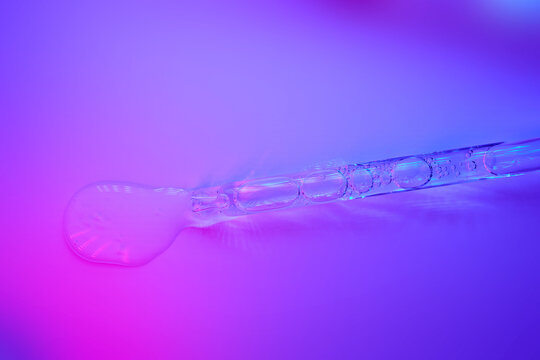 Cosmetic serum dropping from glass pipette on vibrant surface