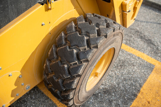 Close-up of a wheel with a heavy-duty lugged tire on a Bobcat skid-steer loader or yellow industrial earthmoving and construction machine; industrial road tires
