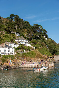 Polperro Cornwall England UK. 13.08.2026. People enjoy a sunny day  in Polperro at a harbour with a small boat and swimming area,
