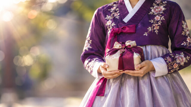 Korean woman in hanbok holding wrapped chuseok gift, silk bojagi present tied with decorative knot, traditional harvest holiday giving for family gratitude celebration
