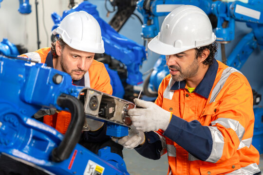 Industrial engineers maintaining and repairing robotic arm machinery in smart factory, automation technicians working together to assemble and test robot arm in manufacturing plant