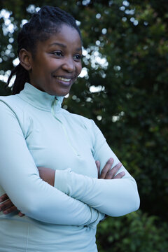 Woman standing in park with arms crossed wearing teal zip-up top, hair in locs, smiling