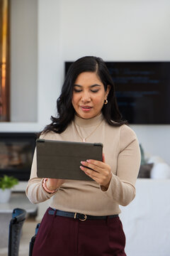 Woman standing in modern living room holding tablet in folio case wearing beige sweater
