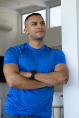 Obraz premium African American man standing arms crossed in living room in blue athletic shirt looking up left