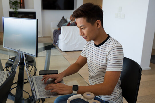 Male housemates working and relaxing in living room with laptop, monitor, headphones, smartwatch