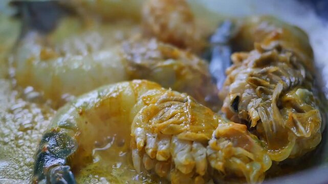 Close up shot of fresh raw prawns cooking in a pan with bubbling oil and spices, creating a delicious meal in motion