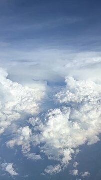 Expansive view of fluffy white clouds against a blue sky captured from an airplane window during daytime flight over a serene landscape. Slow motion vertical footage, 4K, copyspace