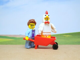 Fototapeta premium Indonesia - January 4, 2026 : Mini toy of action figure at outdoor with blur background. Miniature photography concept design. Minifigure of farmer with chicken at red wheelbarrow. Agriculture theme.
