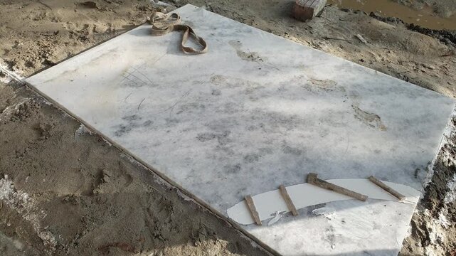 White marble slab slab resting on ground at construction site with stone pieces and lifting strap