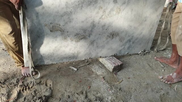 Two construction workers carefully lifting and moving a heavy marble slab manually at a building site.