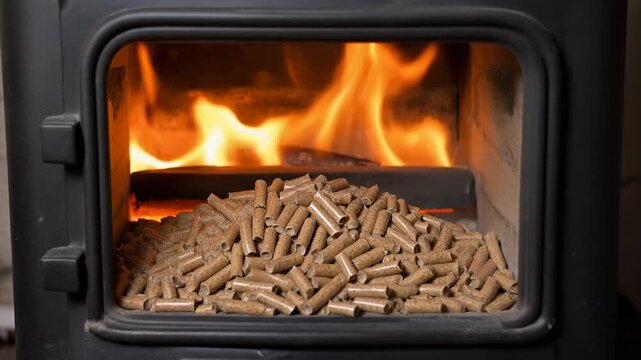 Close view of wood pellets inside burning cast iron stove with moving flames