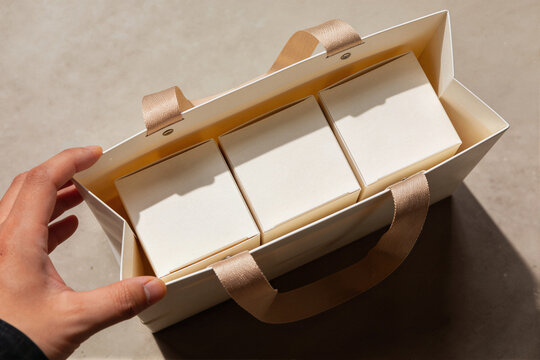 Hand holding an open white gift box containing three smaller white boxes inside