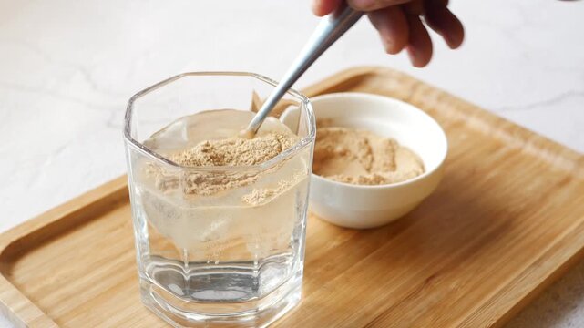 Hand pours powder from spoon into glass of water for mixing drink footage