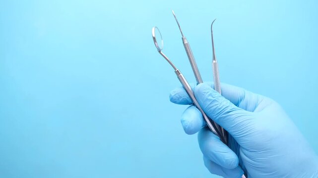 Gloved hand holding dental tools against blue background including mirror and scalers for oral hygiene