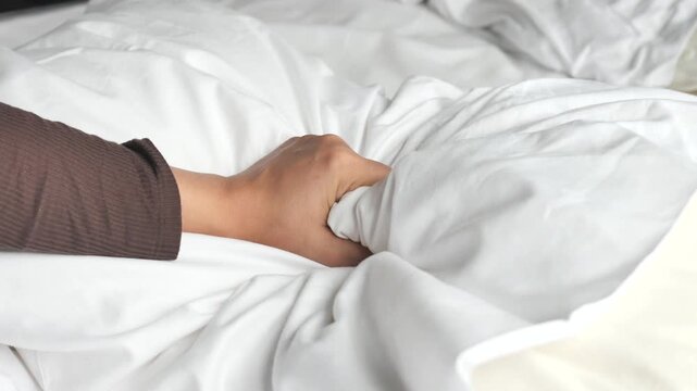 Hand grasping soft white duvet in bed conveying comfort relaxation and gentle morning scene