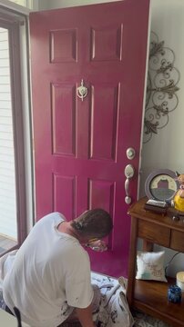 Handyman painting lower portion of the front door of a house 