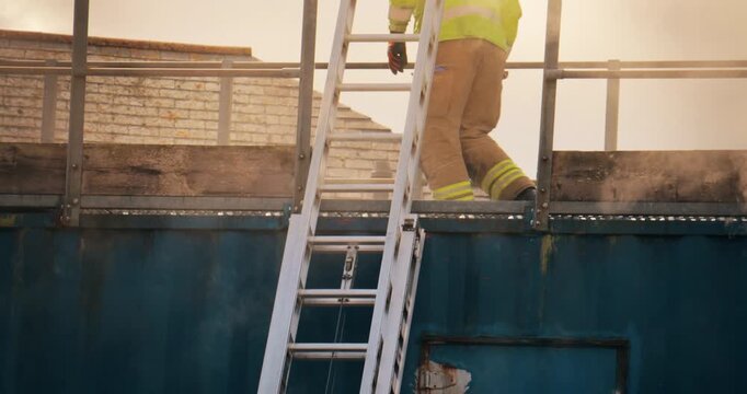 Firefighter crew &ndash; emergency service fireman rescue in action. In uniform in response to fire with firefighting ladder against burning building releasing smoke.